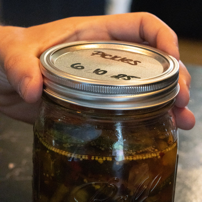 Hand holding a wide-mouth glass jar filled with homemade pickles sealed with a metal canning lid and band featuring BPA-free sealing compound, perfect for Kitchen & Food, Food Preservation, Canning, Canning Jar Lids and Bands, and Best Sellers collections.