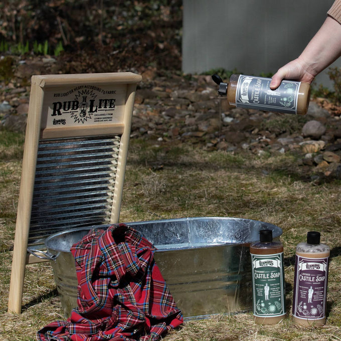 Handcrafted Lehman's Castile concentrated soap bottles placed near a metal wash tub with a washboard and a red plaid shirt, highlighting natural, multi-use soap in Health & Wellness, Grooming, Soaps, USA Made, and Best Sellers collections.