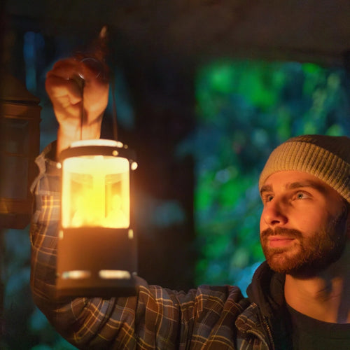 Young man wearing a knit cap holding a glowing handcrafted Candlelier Candle Lantern indoors, illuminating his face with warm light, ideal for camping, emergency, and outdoor use.