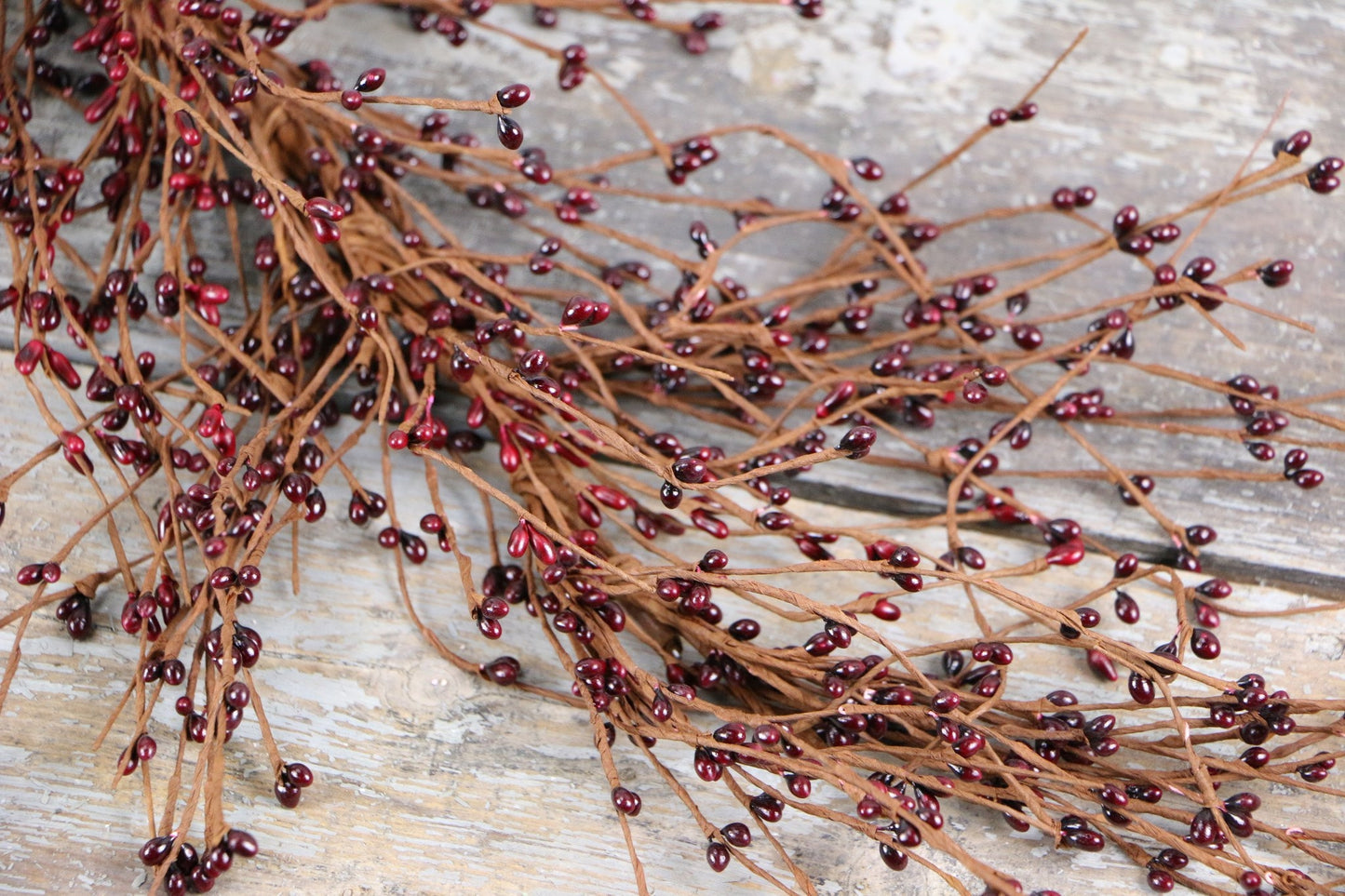 Close-up of decorative brown branches with small dark red berries arranged on a rustic wooden surface, evoking a natural, earthy aesthetic.