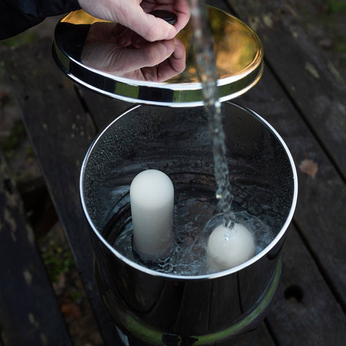 Handcrafted stainless steel gravity filter with dual ceramic elements being filled with water, ideal for camping, emergency supplies, and farm, garden & tool uses.