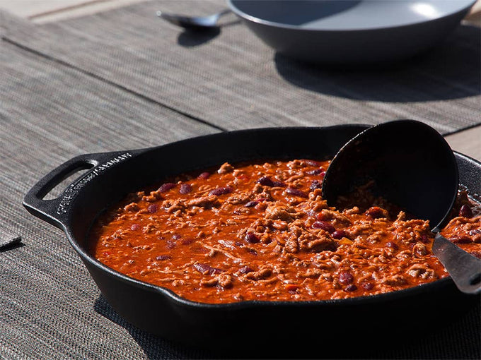 Cast iron skillet with long handle filled with seasoned chili containing beans and ground meat on a woven placemat, ideal for Farm, Garden & Tool, Kitchen & Food, Camping, Cookware, Cast Iron, and Best Sellers collections.