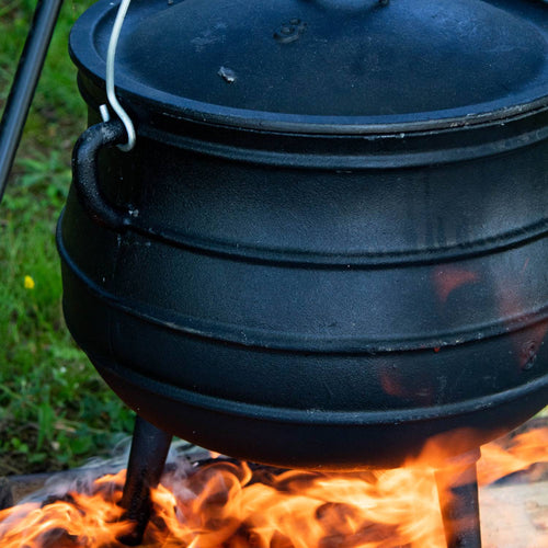Handcrafted cast iron campfire kettle with sturdy legs and round lid, sitting over an open campfire, ideal for outdoor cooking in Farm, Garden & Tool, Camping, Best Sellers, and Promo Eligible collections.