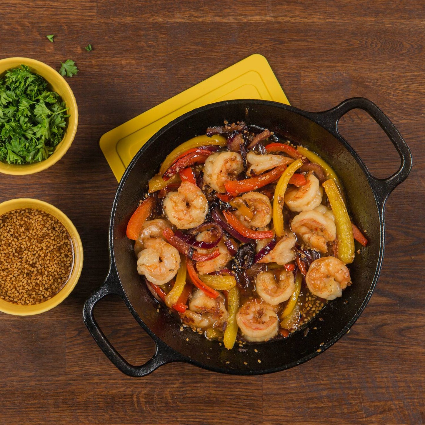 Handcrafted cast iron round pan with short side handles cooking sautéed shrimp with red, yellow, and orange bell peppers, accompanied by bowls of fresh herbs and seeds, ideal for Kitchen & Food, Cookware, Cast Iron, Best Sellers, Promo Eligible collections.