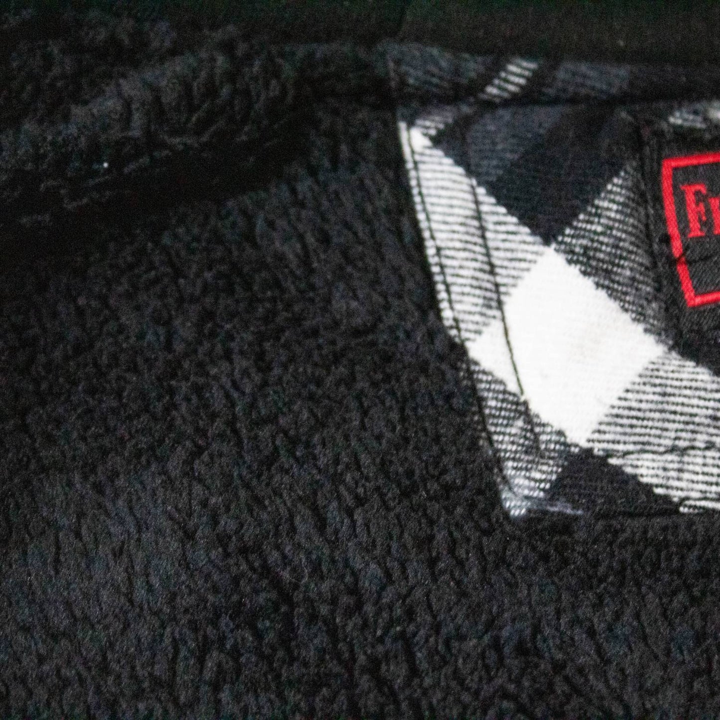 Close-up view of a black sherpa lining with a glimpse of black and white plaid flannel fabric, showcasing plush texture and handcrafted quality in clothing and health collections.