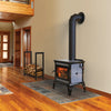 Wood heat stove with dark gray stone panels and black cast iron frame, featuring a visible warm fire through the front glass, placed on a tile hearth in a wood-floored room, part of Stoves and Best Sellers collections.