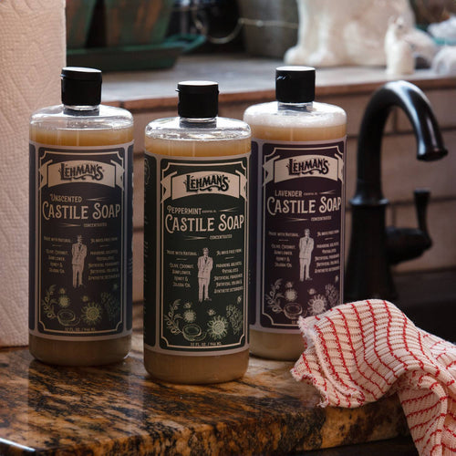 Three handcrafted Lehman's Castile soap bottles in unscented, peppermint, and lavender varieties displayed on a kitchen countertop near a black faucet, highlighting USA made natural liquid soaps for health and grooming collections.