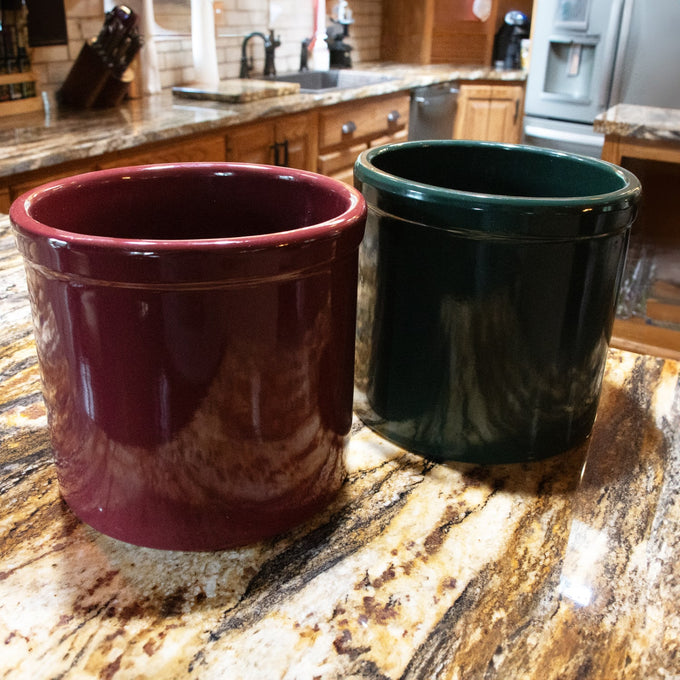 Two handcrafted stoneware crocks in deep red and green colors, designed for fermenting and food preservation, featured in Kitchen & Food, USA Made, and Best Sellers collections.