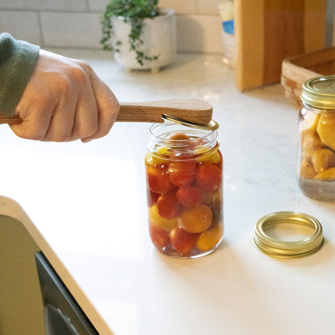 Handcrafted wooden jar spatula lifting canning jar lid from a glass jar filled with colorful tomatoes, showcasing a unique kitchen tool in Food Preservation and Canning collections.