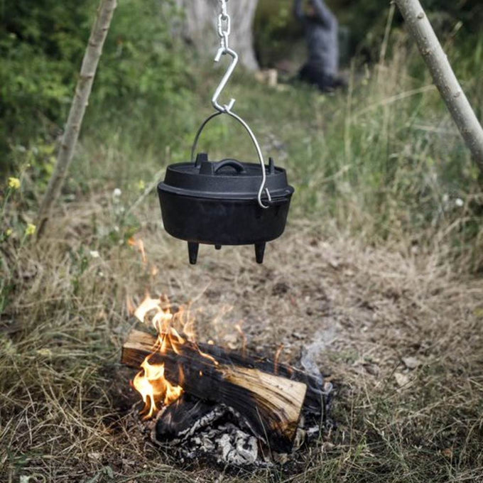 Black cast iron Dutch oven with three legs and a bail handle, suspended over an open campfire for outdoor cooking, ideal for Kitchen & Food, Cookware, Cast Iron, Best Sellers, and Promo Eligible collections.