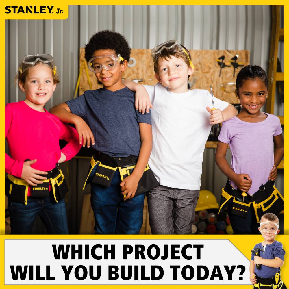 Group of four children wearing safety goggles and tool belts posing confidently in a workshop setting, promoting hands-on indoor play and creative building with wooden toys and arts and crafts.