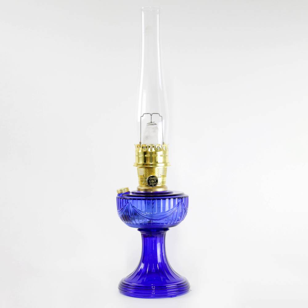 Handcrafted cobalt glass oil lamp with brass burner and tall clear chimney, featuring a Lincoln drape pattern, ideal for Lamps & Lighting, Oil Lamps, Table Lamps, Best Sellers, and Promo Eligible collections.