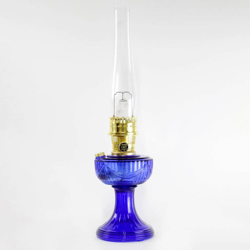 Handcrafted cobalt glass oil lamp with brass burner and tall clear chimney, featuring a Lincoln drape pattern, ideal for Lamps & Lighting, Oil Lamps, Table Lamps, Best Sellers, and Promo Eligible collections.