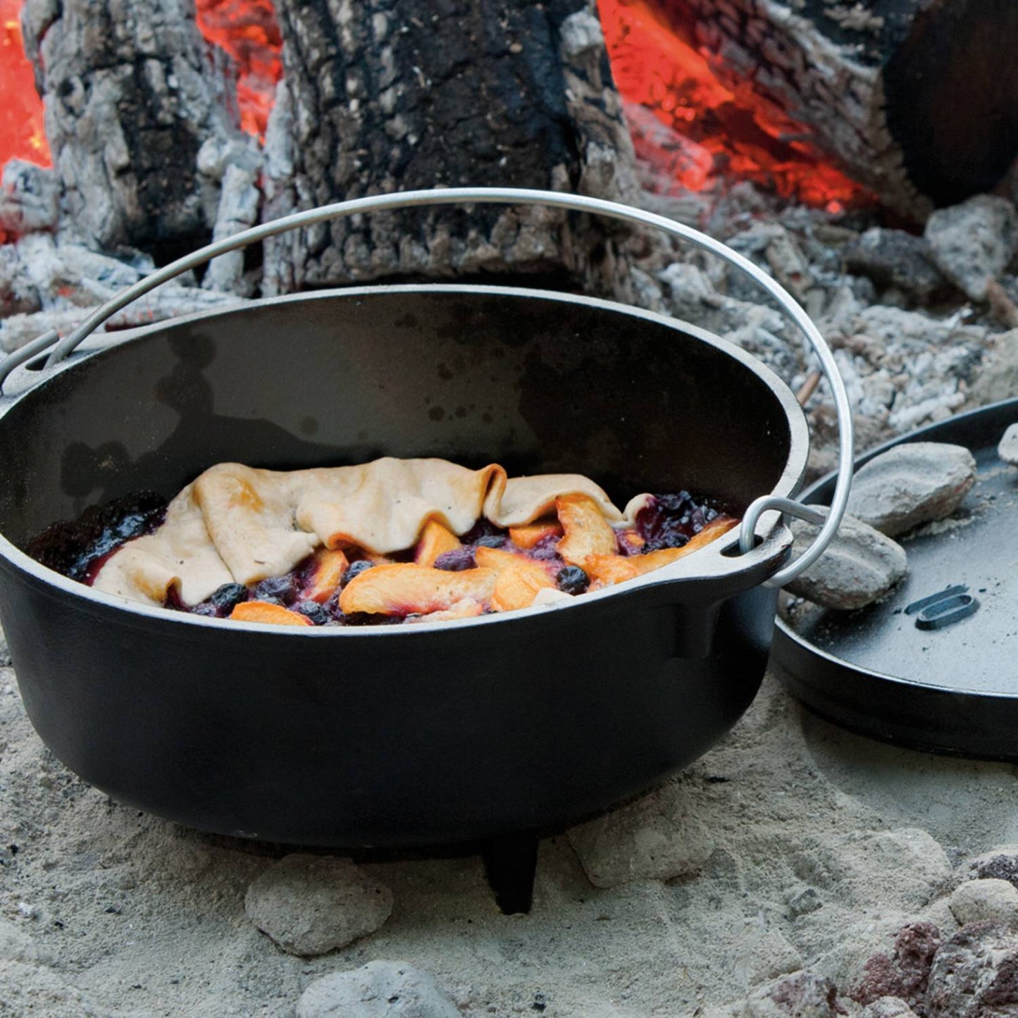 Handcrafted cast iron camp Dutch oven with built-in legs cooking fruit cobbler over open campfire coals, ideal for Farm, Garden & Tool, Camping, Cast Iron, USA Made, and Best Sellers collections.