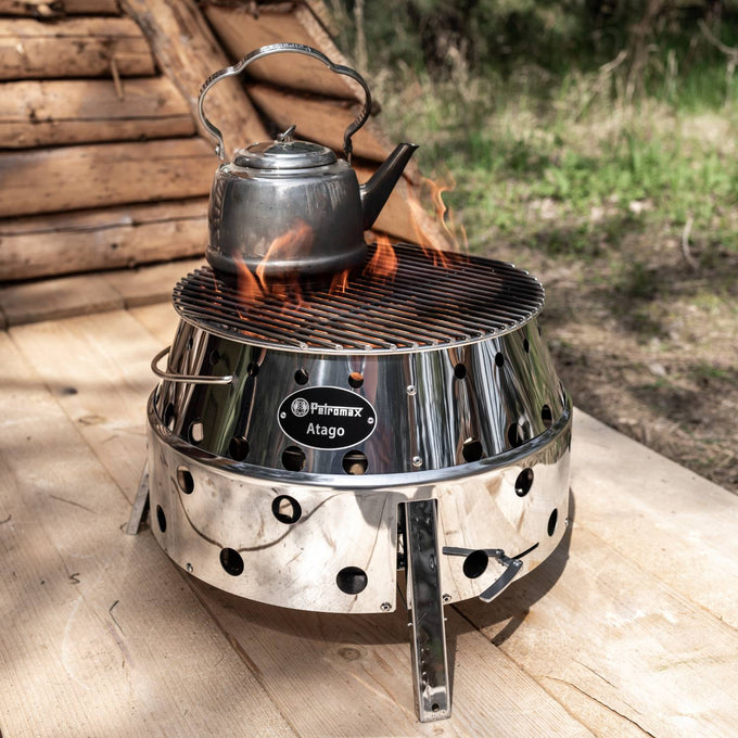Stainless steel teakettle heating over an open flame on a polished metal outdoor fire pit grill, ideal for Farm, Garden & Tool, Camping, Brewing Coffee and Tea, and Kitchen & Food collections.