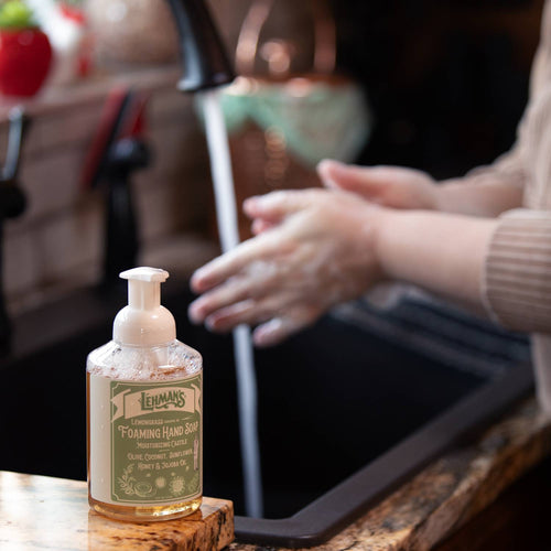 Clear pump bottle of Lehman's handcrafted moisturizing foaming hand soap with a natural formula featuring olive, coconut, sunflower, jojoba oils, and honey, made in USA, shown by a kitchen sink preparing for hand washing, perfect for Health & Wellness and Grooming collections.