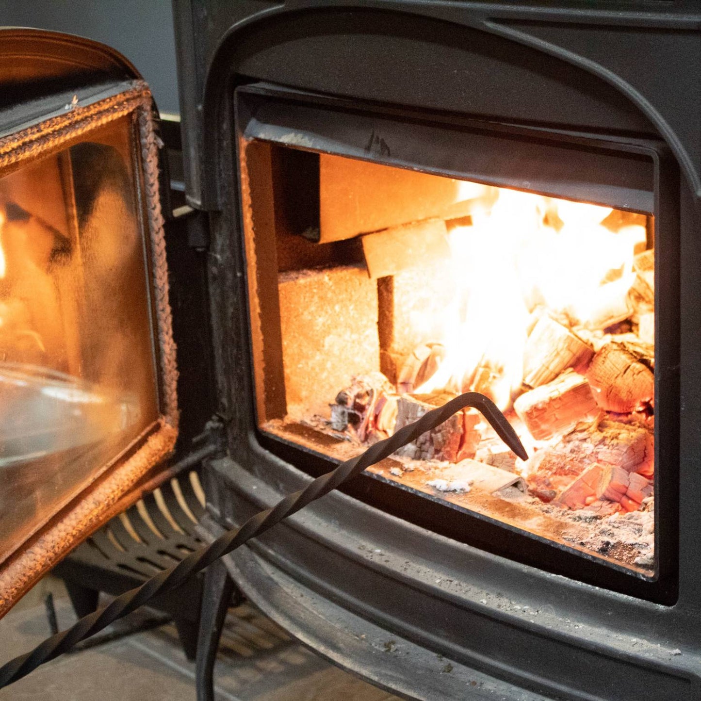 Twisted steel fire poker with a loop handle, Amish made in the USA, shown adjusting logs inside a wood-burning stove, part of Stoves, Hearth Accessories, and Best Sellers collections.