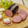 Smoky, handcrafted summer sausage from Amish Country with slices arranged on a wooden board alongside crackers, herb cheese, and green grapes, perfect for Kitchen & Food and Snacks and Sweets collections.