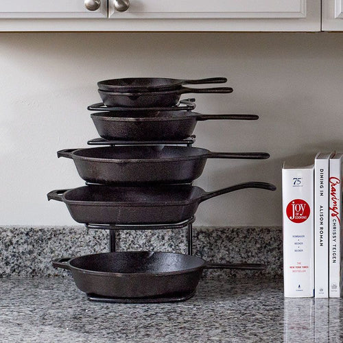 Stack of black cast iron skillets arranged on a sturdy five-tier steel organizer on a kitchen countertop, next to cookbooks, perfect for Kitchen & Food and Storage collections.