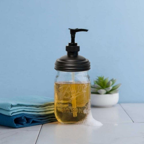 Clear glass regular-mouth mason jar filled with golden soap and topped with a durable black pump lid, set on a white surface with folded blue towels and a small green succulent, ideal for Health & Wellness, Home & Decor, Soaps and Soapmaking, and USA Made collections.