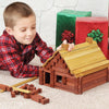 Young boy playing indoors with handcrafted Amish made wooden log set building a detailed cabin next to wrapped holiday gifts, part of USA made children's toys collections.